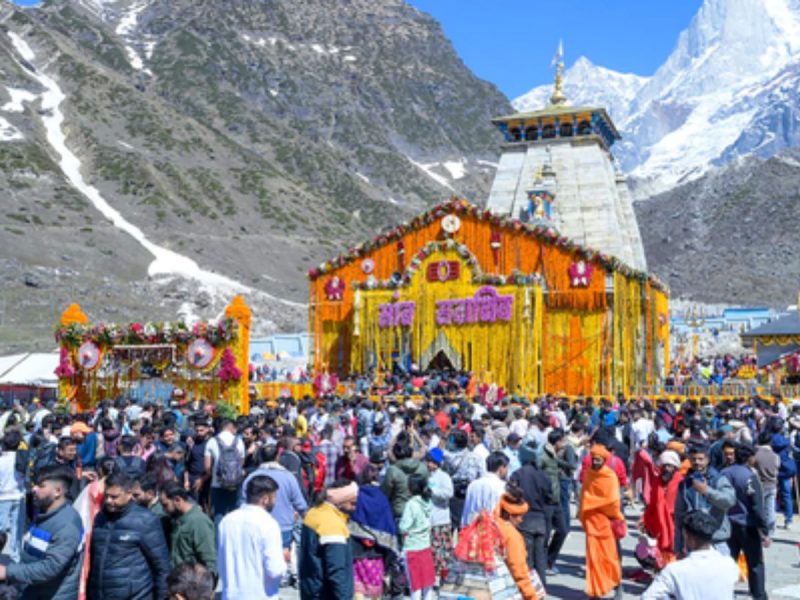 Crowd gathers at a brightly decorated temple structure set against snowy mountains during a festival.