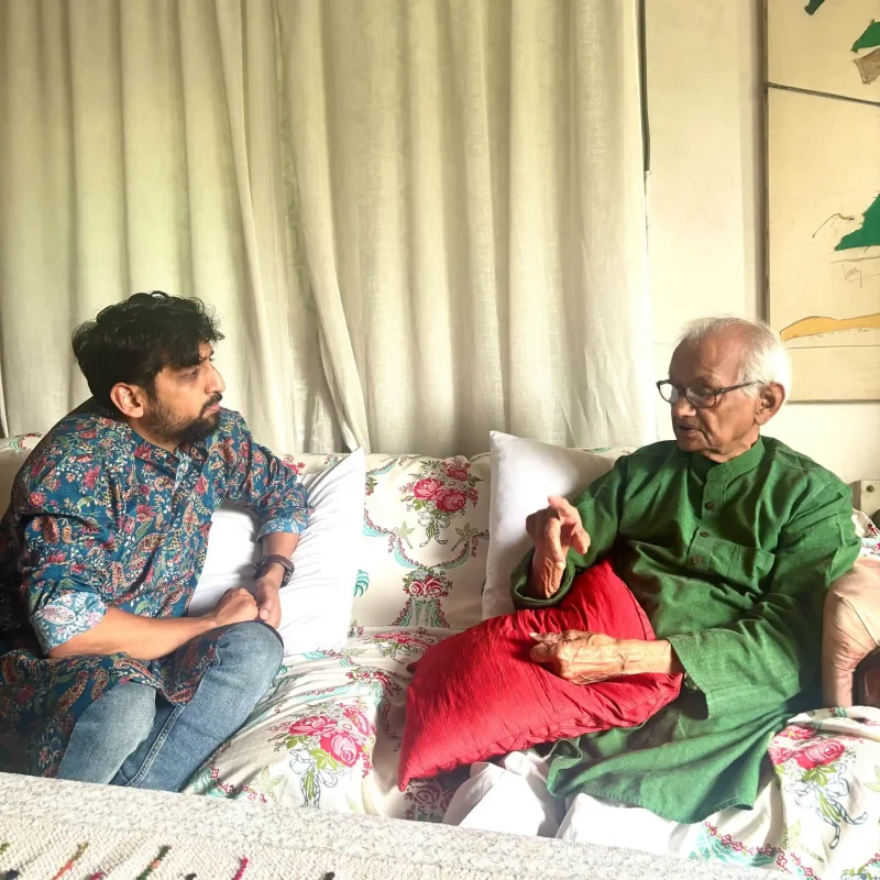 Discussion with Naresh ji - bolebharat Two men seated on a floral sofa indoors, conversing with each other on a bright living room backdrop.