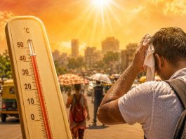 Wooden thermometer shows high temperature beside a man wiping sweat from his face in a sunny, crowded street market.