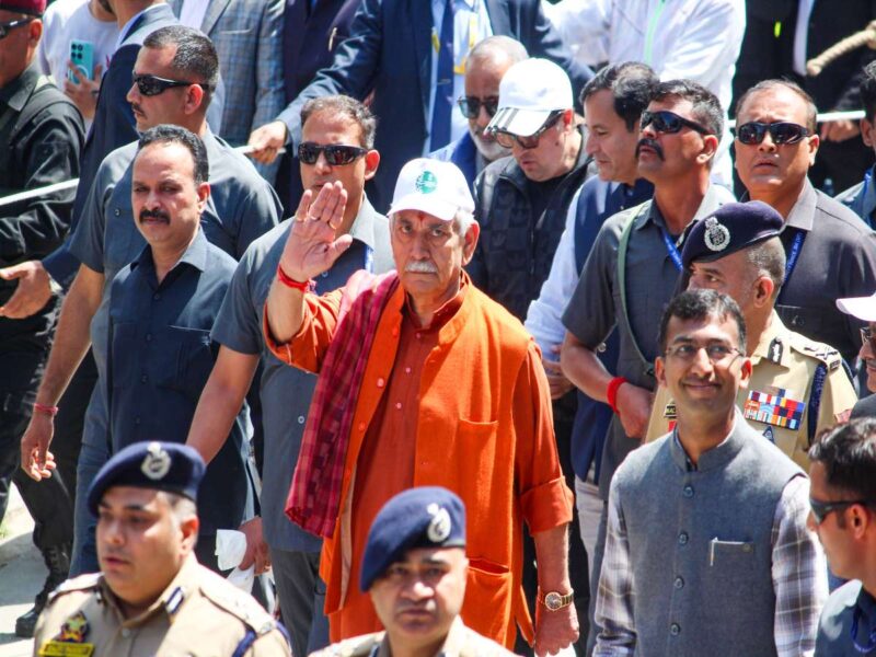 Man in an orange kurta waving at a crowd, surrounded by security and officials outdoors.