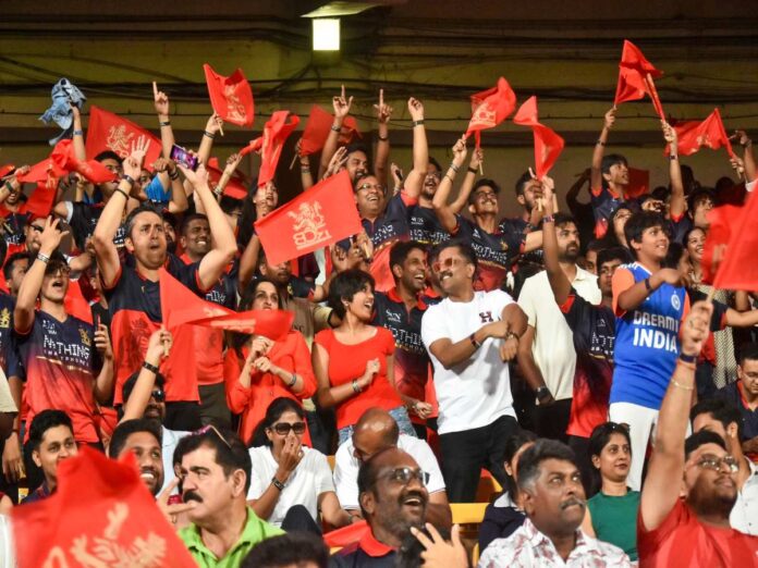 Crowd of sports fans waving red flags and cheering in a stadium, many wearing matching dark shirts and team colors.