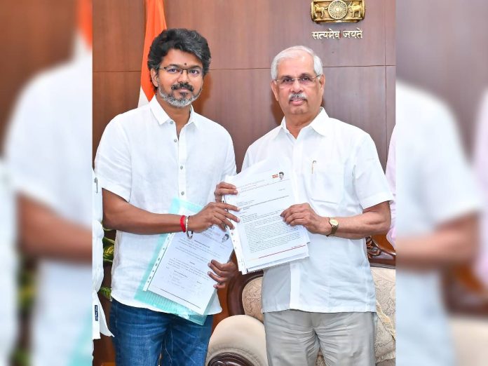 Two men in white shirts exchange documents in an official setting with a government emblem behind them.