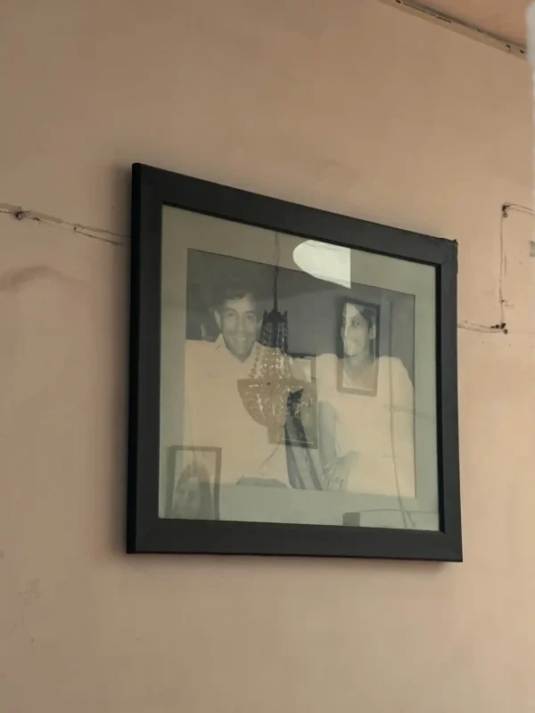 Young Naresh ji and Wife - bolebharat Angled black-framed photo collage hanging on a beige wall, showing grayscale portraits inside the frame.