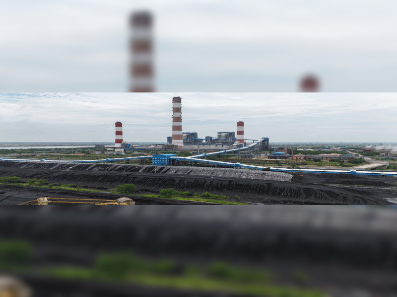 Large coal power plant with three red-and-white striped smokestacks and blue conveyor systems on a flat industrial landscape.