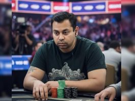 Man sits at a poker table concentrating, wearing a dark green shirt and headphones, with poker chips stacked in front of him (red, green, black).