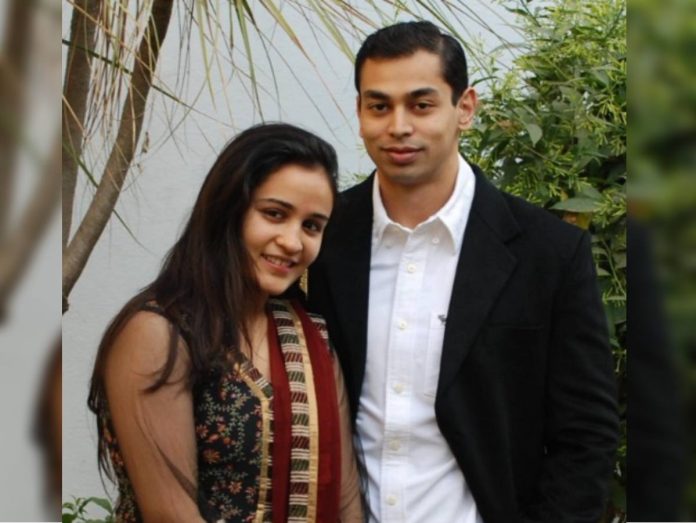 Smiling couple posing outdoors with greenery in the background.