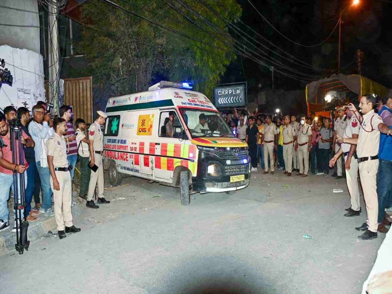 Ambulance driving through a crowd at night with police and bystanders watching on both sides of the street.
