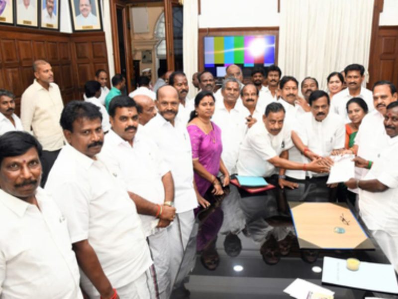 Group of Indian colleagues in white shirts around a table as a document is handed over in a formal setting