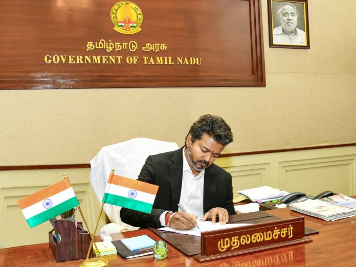 Government official signs documents at a Tamil Nadu government office desk with Indian flags nearby