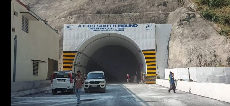 Tunnel entrance labeled AT-03 SOUTH BOUND with yellow-black safety stripes and vehicles nearby on a road under construction.
