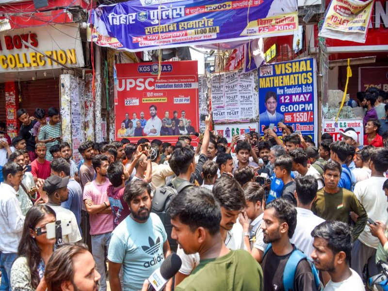 Large crowd of young people gathers in a busy street with colorful posters and banners advertising UPSC coaching and a new foundation batch for Visnal Mathematics.