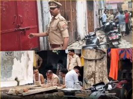 Police officers in khaki uniforms inspect a narrow street near a red door, with motorcycles parked along the curb.