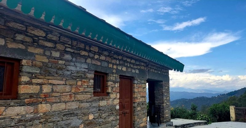 Stone house with a green scalloped awning, brown door and window, and a distant mountain valley. (outdoor scene)