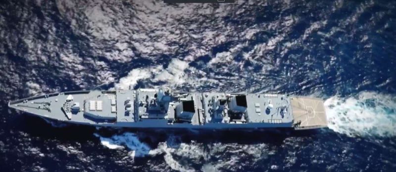 army yoga - bolebharat Top-down view of a gray military warship cruising through open ocean, with wake trailing on both sides and deck structures visible.