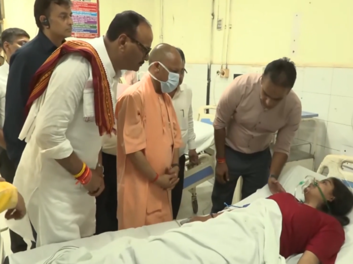 Group of men stand around a hospital bed as a patient lies with an oxygen mask, being attended by a person leaning over the bed.
