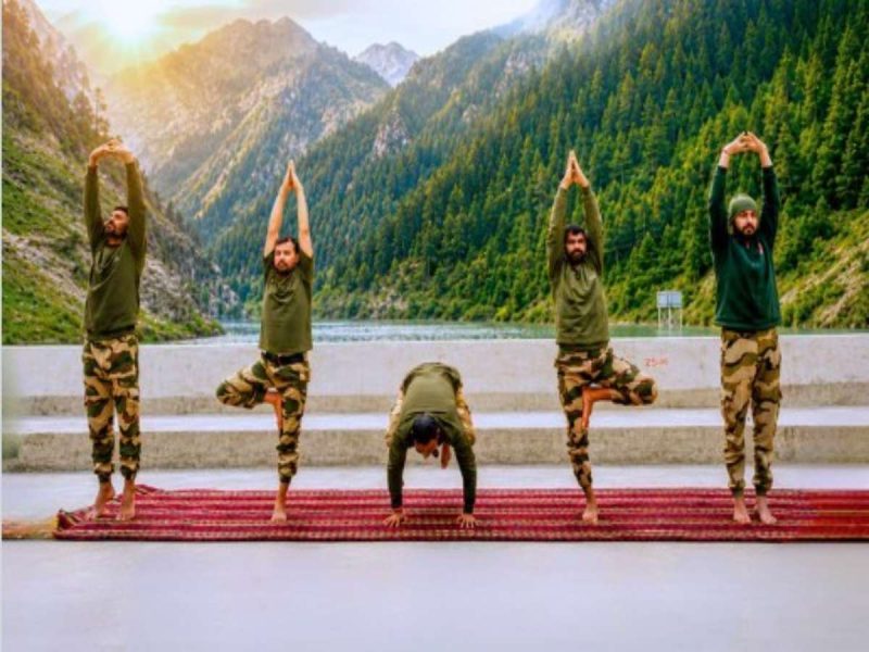 crpf - bolebharat Group of five men in green shirts and camouflage pants doing yoga on a red mat outdoors in a mountain valley.