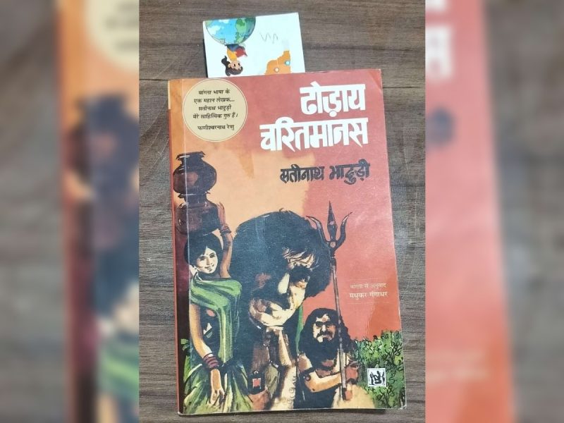 Hindi book cover with bold white title at the top, orange background, and a central illustration of mythic figures including a bearded man and a figure with a trident, plus a woman in a green sari on the left and greenery at the bottom right.