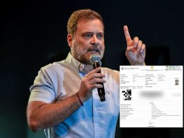 Man with short hair and beard speaks into a handheld microphone on stage, raising his index finger as if making a point.