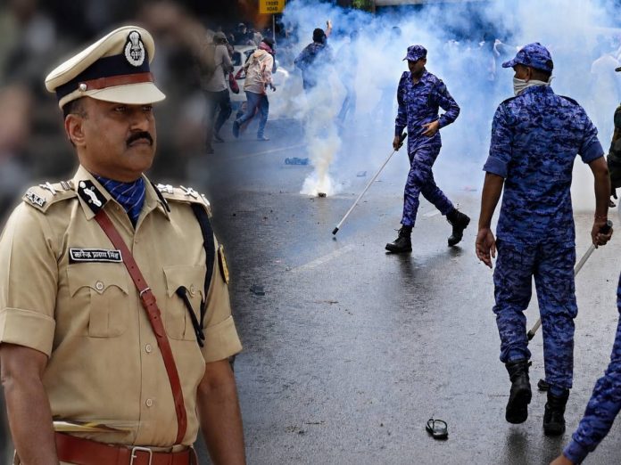 Police officer in a khaki uniform foreground as protesters and blue smoke fill a street behind him used during a clash with riot police in blue camouflage.