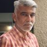 Portrait of a middle-aged man with gray hair and a light beard, wearing a pink plaid shirt, looking at the camera.