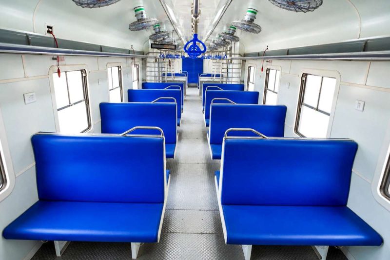 Interior of a train car with blue seats facing each other along a central aisle, windows on the sides.