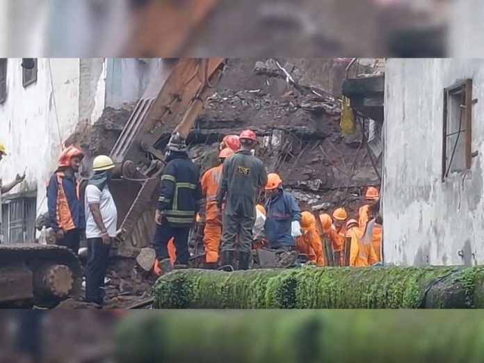 Rescue workers in orange overalls and hard hats search through rubble at a collapsed building site with heavy machinery nearby.