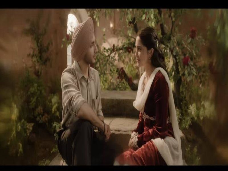 main wapas aaunga film - bolebharat Man wearing a turban sits on steps and chats with a woman in a red traditional dress and white scarf in a lush garden.