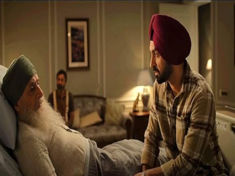 main wapas aaunga movie - bolebharat A younger Sikh man in a plaid shirt sits beside an elderly man with a long white beard in a hospital bed, holding his hand in a dimly lit room.