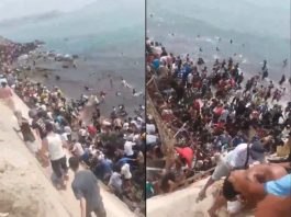 स्पेन के सेउटा में करीब 50,000 प्रवासी घुसे, मोरक्को सीमा पार करते समय 18 की मौत; हालात काबू करने के लिए भेजी गई सेना Large crowd lined up along a concrete sea wall at the shore, with people standing in the water and on the steps by the beach.