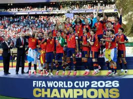 FIFA World Cup: स्पेन 16 साल बाद फिर बना फुटबॉल का बादशाह, अर्जेंटीना को 1-0 से हराकर दूसरी बार बना चैंपियन Spain national football team celebrates on the podium with trophy and medals after winning the FIFA World Cup 2026, fans in background.