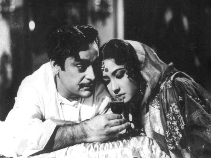 Man and woman in traditional Indian dress sit close together, sharing a wine glass.