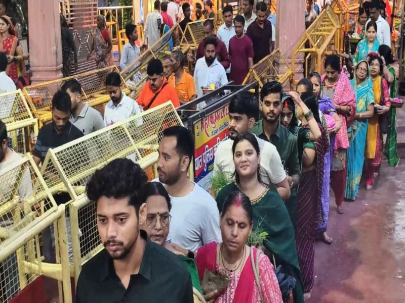 Crowd of people in colorful traditional clothing standing in a long queue beside yellow metal barricades outside a temple or shrine.