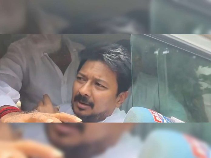 Man with dark hair and beard leaning out of a car window, speaking to reporters, microphones in the foreground.